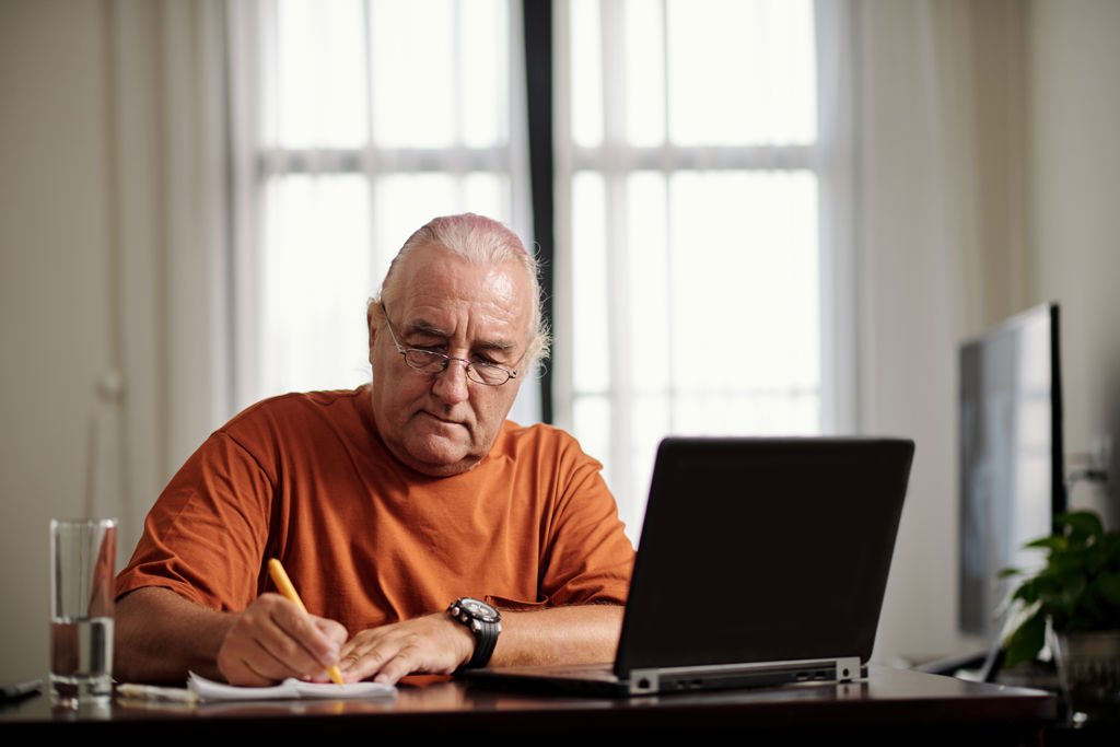 Senior man achter computer in huis. 
