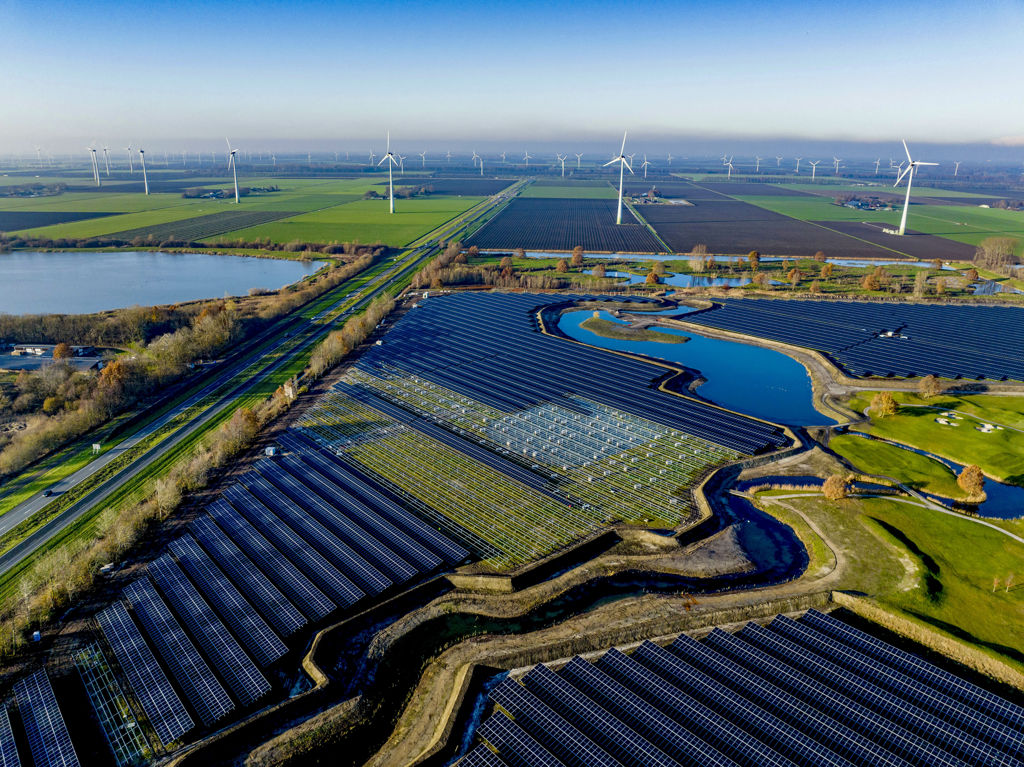 Landschap Nederland met windmolens en grasvelden met zonnepanelen.