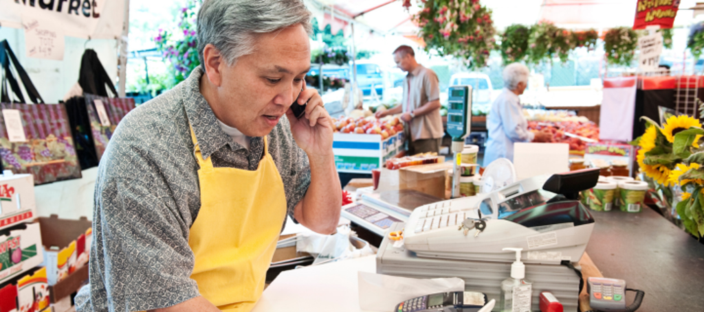 eigenaar van winkel achter de kassa met telefoon in zijn hand