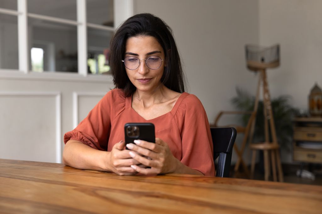 Vrouw kijkt op telefoon in huis. 