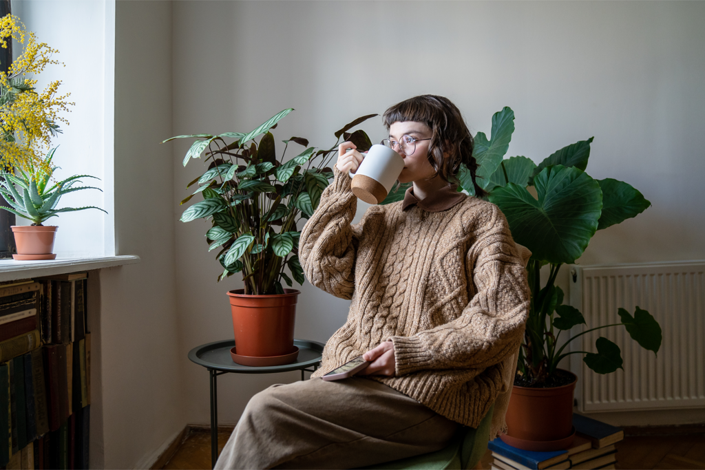 Vrouw met kop thee in stoel, kijkend naar buiten.